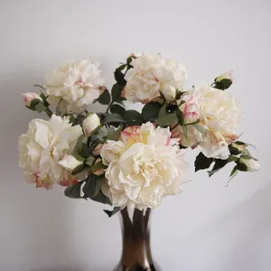 Elegant cream artificial peonies with pink edges in a stylish glass vase for home decor.