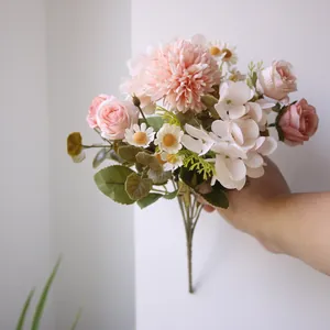 Detailansicht einer Hand, die einen künstlichen Blumenstrauß vor einer weißen Wand hält.