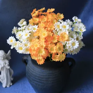 Close-up of vibrant orange and white artificial daisies in a vintage blue vase