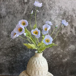 Amapolas de Islandia artificiales azul claro colocadas en un jarrón de cerámica crema texturizado.