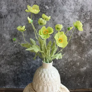 Detalle de flores de seda de amapola de Islandia artificiales en un jarrón de cerámica blanca.
