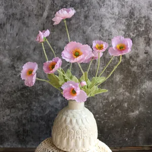 Primer plano de amapolas de Islandia artificiales rosas con tallos peludos en jarrón blanco.