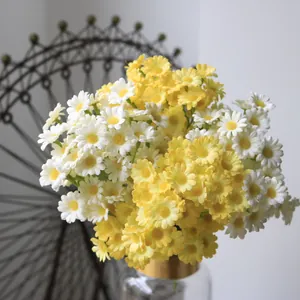 Close-up view of bright yellow and white artificial daisies in a gold-rimmed glass vase