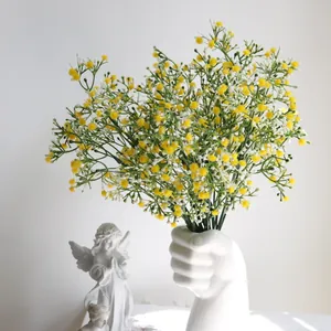 Gipsofila amarilla artificial en un jarrón de cerámica blanca con forma de puño.