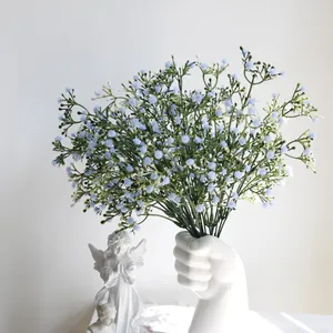 Elegante ramo de paniculata artificial azul claro en un creativo jarrón blanco con forma de mano.