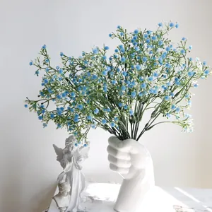 Primer plano de flores de paniculata artificial azul en un jarrón de cerámica blanco