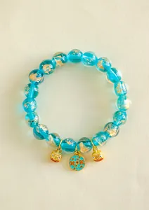 Detail von blauem Glasperlenarmband mit goldenen Fabelwesen-Anhängern