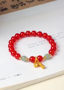 Nahaufnahme eines roten Karneol-Perlenarmbands mit goldenen Anhängern auf antikem Buch