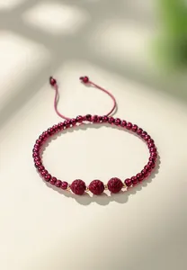 Dettaglio macro di perle di granato e ciondoli in cinabro intagliato su cordino rosso.