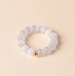 Makroansicht eines minimalistischen weißen Katzenaugenstein-Perlenrings mit goldener Zwischenperle