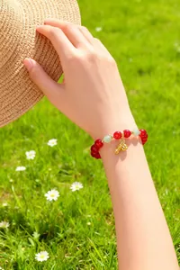 Nahaufnahme einer Hand mit Glücksbringer-Armband aus roten Perlen und goldenen Anhängern im Freien