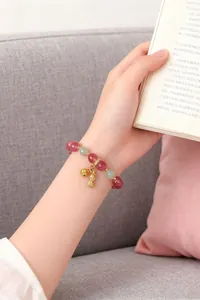 Nahaufnahme eines Armbands aus rosa Kristallen mit Glücks-Erdnuss-Anhänger an der Hand