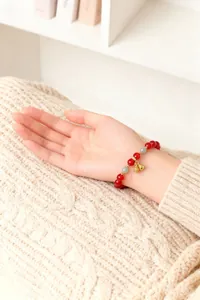 Detailansicht eines rot-grünen Perlenarmbands mit goldenen Glockenanhängern am Arm.