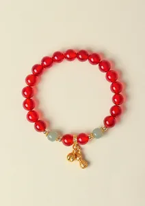Nahaufnahme eines Armbands aus roten Achatperlen mit goldenem Erdnussanhänger auf Beige.