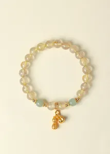 Nahaufnahme von Gold-Rutilquarz-Armband mit Glückserdnuss- und Glockenanhängern
