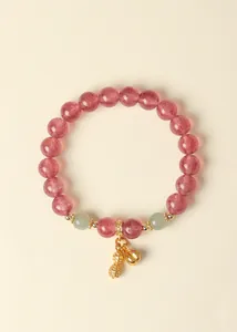 Detailansicht eines rosa Erdbeerquarz-Armbands mit goldenem Erdnuss-Anhänger und Jade.