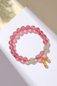 Nahaufnahme eines Armbands aus rosa Erdbeerquarz mit goldenem Erdnussanhänger und Jade