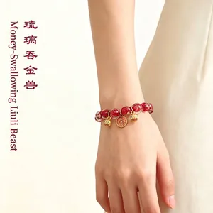 Elegantes rotes Glasperlenarmband mit goldenen Glückstier-Anhängern am weiblichen Handgelenk