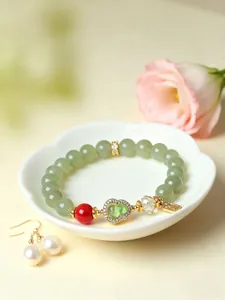 Detailansicht eines grünen Perlenarmbands mit glitzerndem Kürbis-Anhänger und roter Perle.