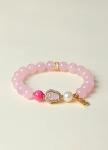 Detailansicht eines Rosenquarz Perlenarmbands mit goldenem Kürbisanhänger und weißer Perle.