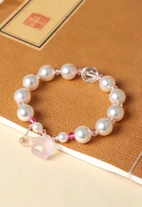 Dettaglio bracciale di perle con ciondolo fiore in quarzo rosa su un taccuino.