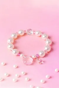 Dettaglio di un dolce braccialetto di cristallo rosa e perle bianche su sfondo rosa