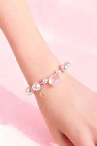 Dettaglio del braccialetto di perle bianche e fiore di cristallo rosa sul polso