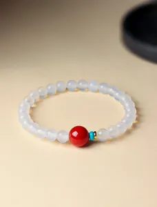 Detailopname van een elegante witte agaat kralenarmband met rode kraal en goud accent