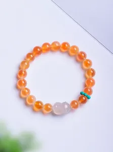 Vue détaillée d'un bracelet en perles d'agate orange avec une fleur de muguet sculptée.