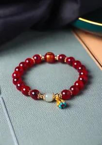 Dettaglio di un bracciale di perle di agata rossa con giada verde e ciondolo a forma di loto.