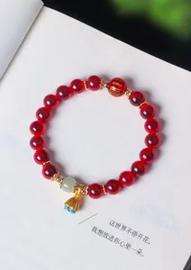 Macro dettagliata di un braccialetto in agata rossa con perla di giada e ciondolo a loto dorato