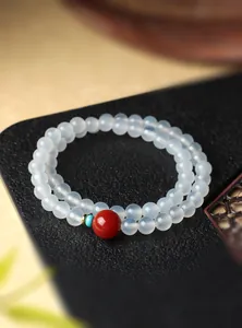 Detailopname van een dubbele witte agaat kralenarmband met een rode accentkraal.