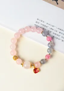 Detailansicht eines Armbands aus rosa und grauen Edelsteinperlen mit rotem Glücksanhänger