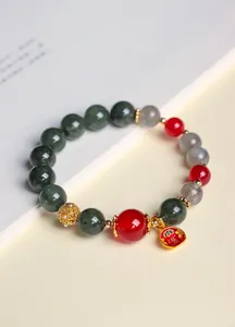 Nahaufnahme eines Armbands aus grünem Rutilquarz und rotem Achat mit goldenem Anhänger.