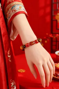 Détail d'un bracelet zodiacal chinois traditionnel en agate rouge et œil de tigre au poignet.