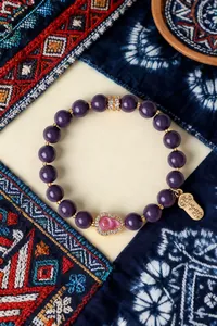 Nahaufnahme eines lila Perlenarmbands mit rosa Pfirsich-Anhänger und Glücksschild
