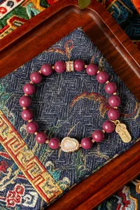 Detailaufnahme eines lila Perlenarmbands mit einem Flaschenkürbis und Glücksanhänger.