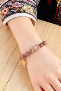 Detailaufnahme eines Armbandes im ethnischen Stil mit rosa Herzstein und Goldanhänger