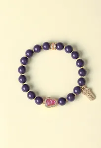 Nahaufnahme eines lila Perlenarmbands mit rosa Kürbis-Anhänger und Glücksbringer