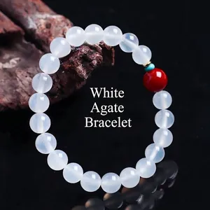 Elegant witte agaat kralen armband met rode gelukskraal op zen houten achtergrond