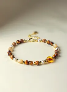 Detail van een armband met natuurlijke zoetwaterparels, tijgeroog en gouden accenten.