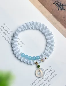 Detailansicht eines weißen Katzenaugenstein-Armbands mit Achat-Anhänger auf einem Buch