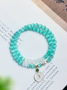 Nahaufnahme eines zweireihigen Katzenaugen-Armbands mit Jade-Anhänger und Perle.