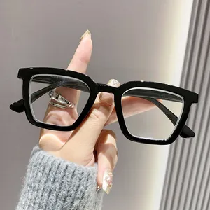 Primer plano de unas modernas gafas de lectura con montura cuadrada negra en mano.