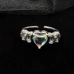Close-up of silver heart moonstone ring with sparkling zircon accents on black background.