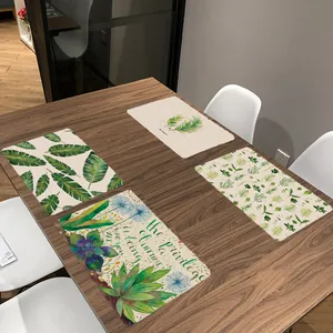 Set van vier placemats met tropische groene bladmotieven op een houten eettafel.