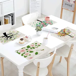 Linen placemats with green plant and floral tree designs on a white dining table setting