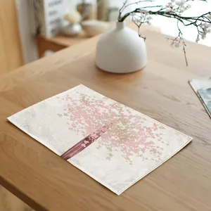 Detailed view of a rectangular linen placemat with pink blossom tree print on a wooden table.