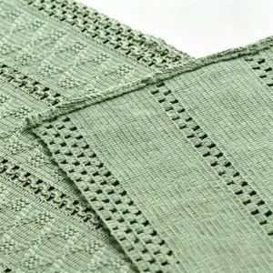 Macro view of sage green woven cotton linen fabric with intricate crochet patterns.