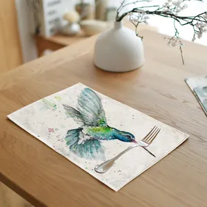 Detailed watercolor hummingbird linen placemat on a wooden dining table with a silver fork.